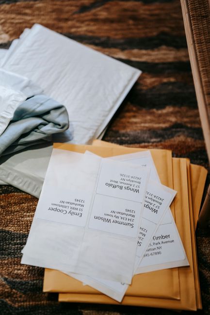 A neatly arranged stack of white and light blue fabric items, possibly linens or wrapping materials, placed on a wooden surface. Resting on top are several folded envelopes and printed notes or ticket
