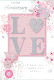 An anniversary card with a softly romantic design is shown as though resting beside a freshly arranged bouquet in an Elmers End living room, capturing the tender mood of a shared celebration. At its heart, the word LOVE appears in bold, raised letters, richly accented with shimmering glitter that glows in silvery highlights, similar to candlelight glinting off a vase of pale pink roses. The tactile quality of the lettering is evident, suggesting a gentle, pleasant roughness to the touch, making the card not only visually appealing but sensorially engaging. Surrounding this central word, a constellation of illustrated flowers unfurls across a blush-pink background, their shapes graceful and stylised, with slender leaves and swirling stems looping elegantly around one another. The blossoms are rendered in a soothing palette of pastel pinks, soft whites, and cool greys, with touches of silver to define certain petals and edges, echoing the careful detail of a florist's work when arranging an anniversary gift. The background shade deepens slightly around the lettering, creating a sense of depth and a subtle spotlight effect, as though the sentiment itself is gently illuminated. Flowing script text weaves through the design, its curves and loops mirroring the natural arc of vines and tendrils, offering warm wishes for a special anniversary moment. The card's overall impression is that of a quiet, intimate tribute to lasting love-perfect to accompany same-day flower delivery across Elmers End and nearby streets-blending the freshness of a spring garden with the timeless elegance of hand-drawn illustration and sparkling, tactile details.